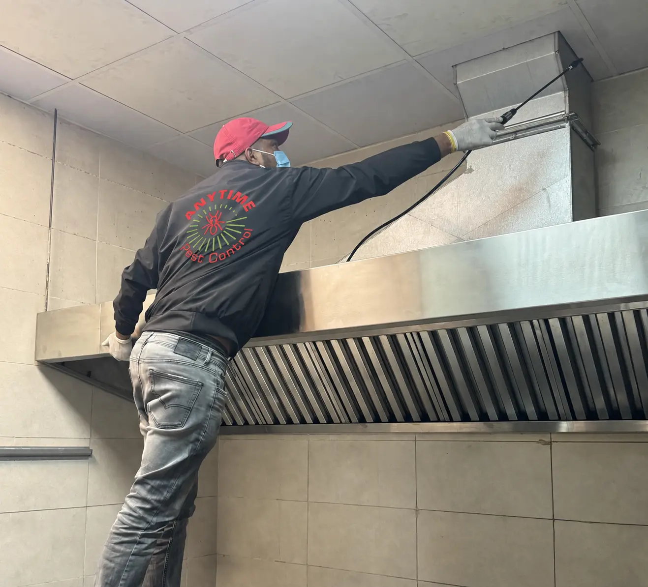 Anytime Pest Control technician treating a commercial kitchen with the company logo on his jacket